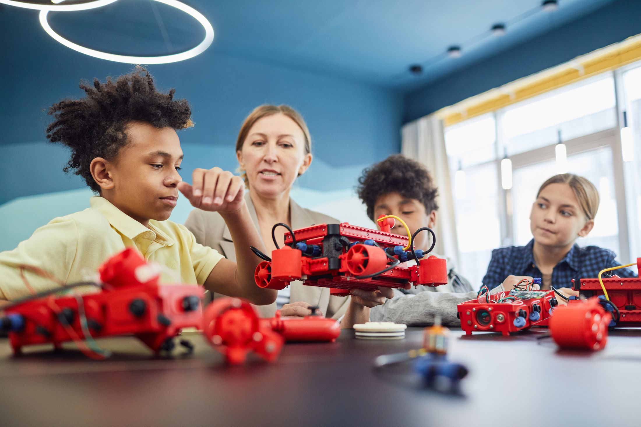 Children and a mentor building a robotics project together at a table.