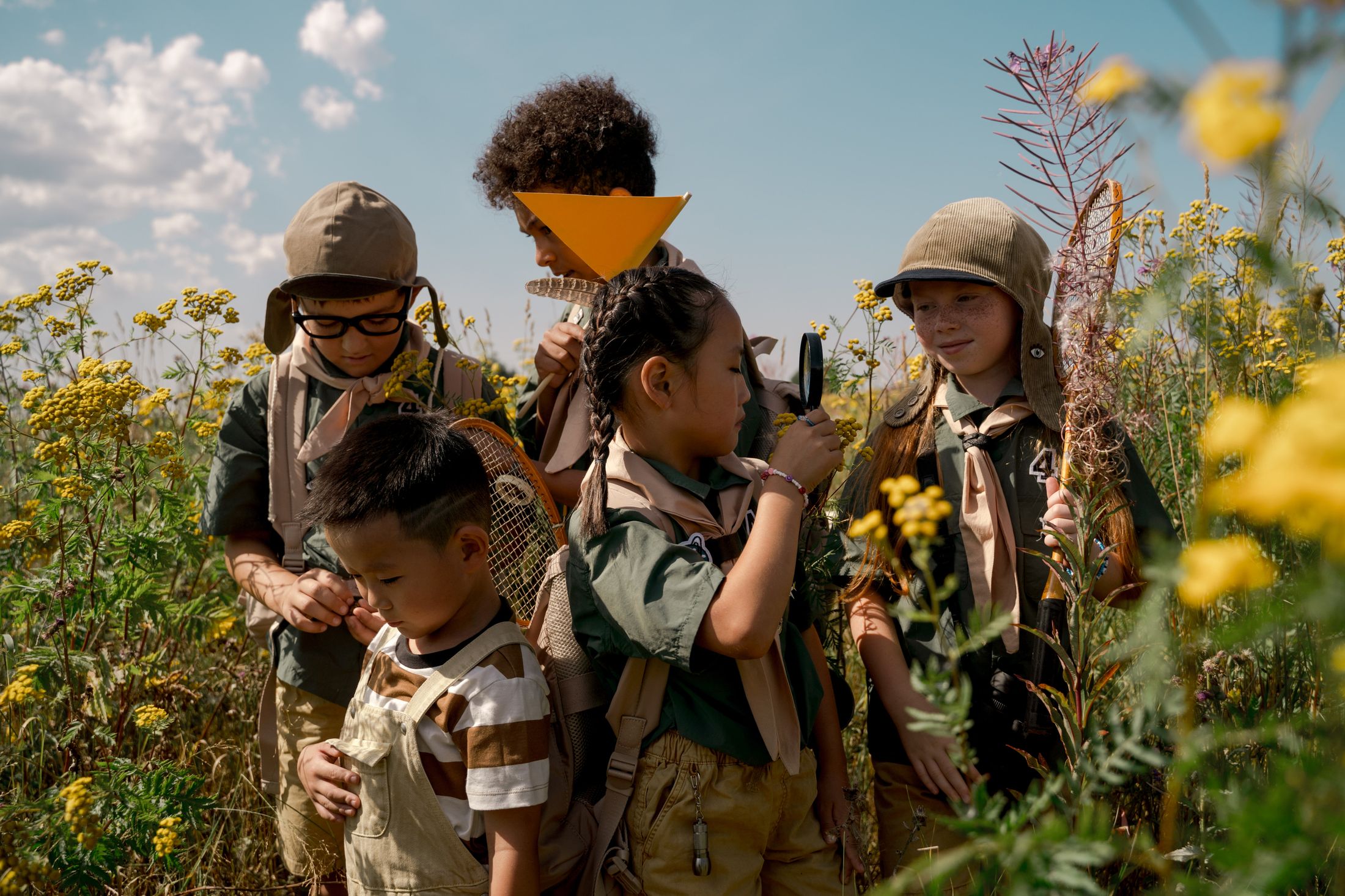 Children exploring plants outdoors with magnifying glasses.